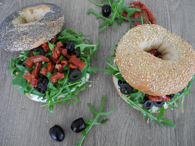Bagel mit Frischkäse, Ruccola, Oliven und getrockneten Tomaten